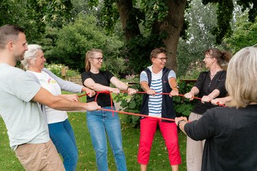 Teilnehmende und Fachbereichsleitung mit einem Seil in der Hand im Kreis stehend