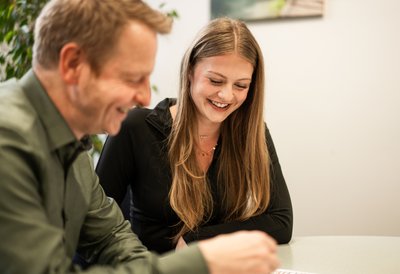 Zwei Personen, eine junge Frau schaut auf eine Liste, ein Mann erklärt sie ihr.